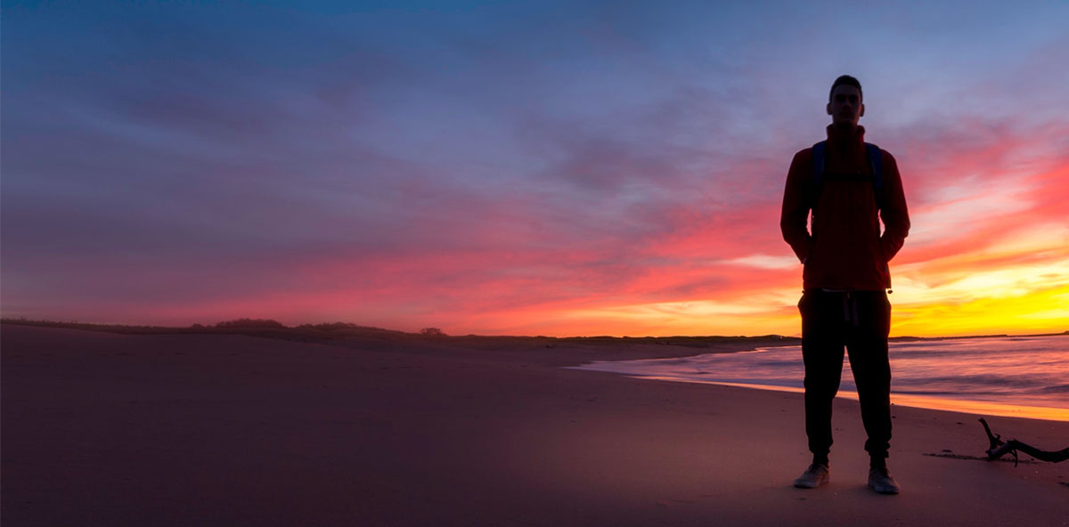 man standing on beach at sunrise
